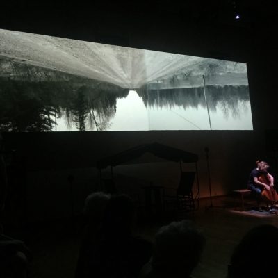 Marie-Hélène Massy-Émond jouant du violoncelle devant une séquence vidéo.